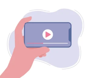 A light pink, stylized hand holds a horizontally oriented smartphone with a light purple screen. On the screen, a white circle containing a pink play button is centered. Below the play button is a white progress bar with a thin red line indicating the playback position. The background features abstract, light purple shapes, suggesting a digital interface or streaming content.