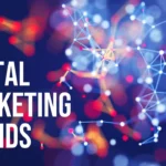 The words 'DIGITAL MARKETING' stacked and left-aligned in large, bold white sans-serif font on the left side of the image. Below, the word 'TRENDS' is in a slightly smaller, bold white sans-serif font. The background is a blurred, abstract representation of a digital network, featuring interconnected white nodes and lines against a dark blue backdrop with bokeh effects in shades of red, orange, and light blue, suggesting technology and interconnectedness in the context of marketing.